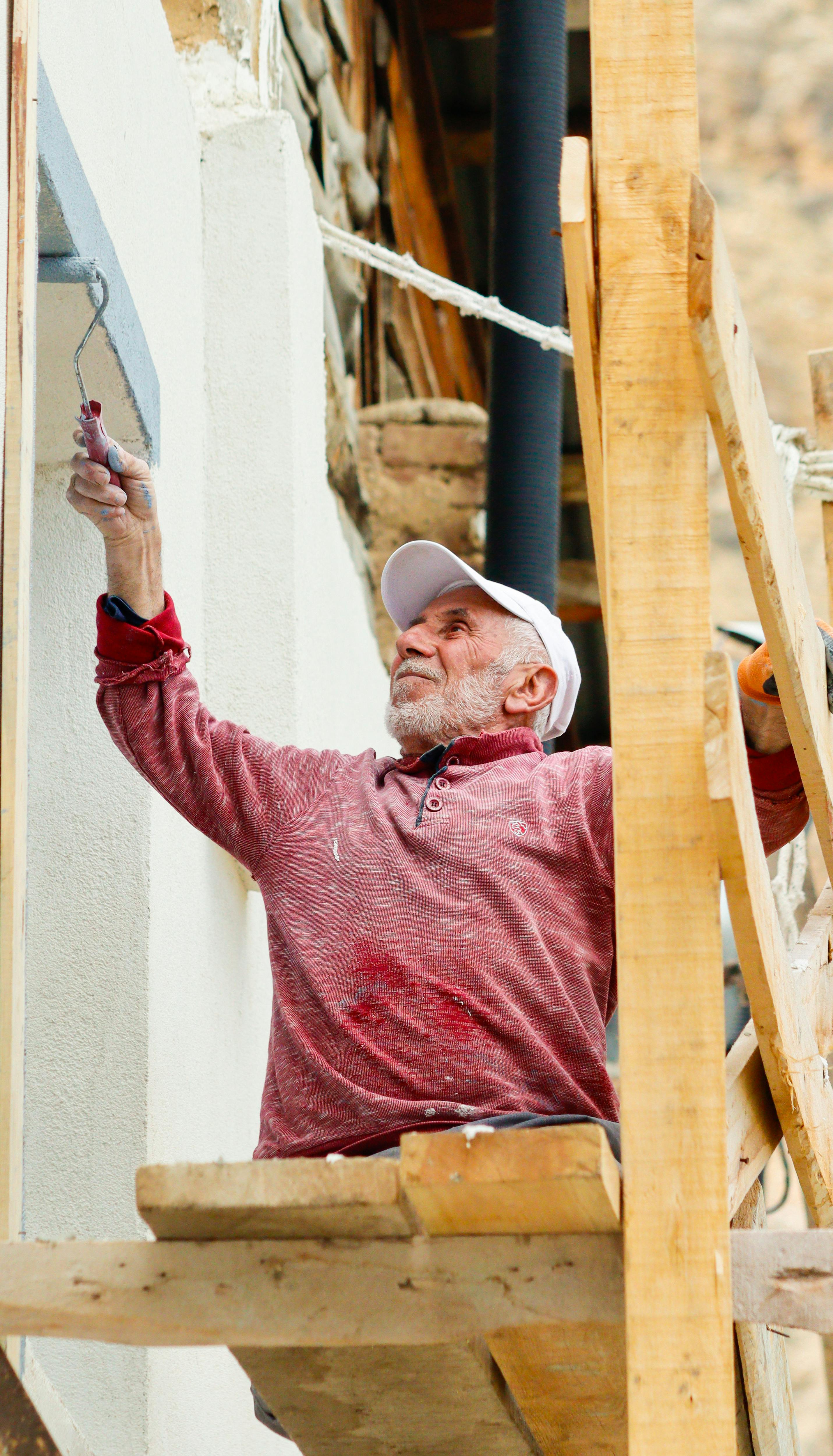 Painter on scaffolding applying paint to an exterior wall — tradesperson at work